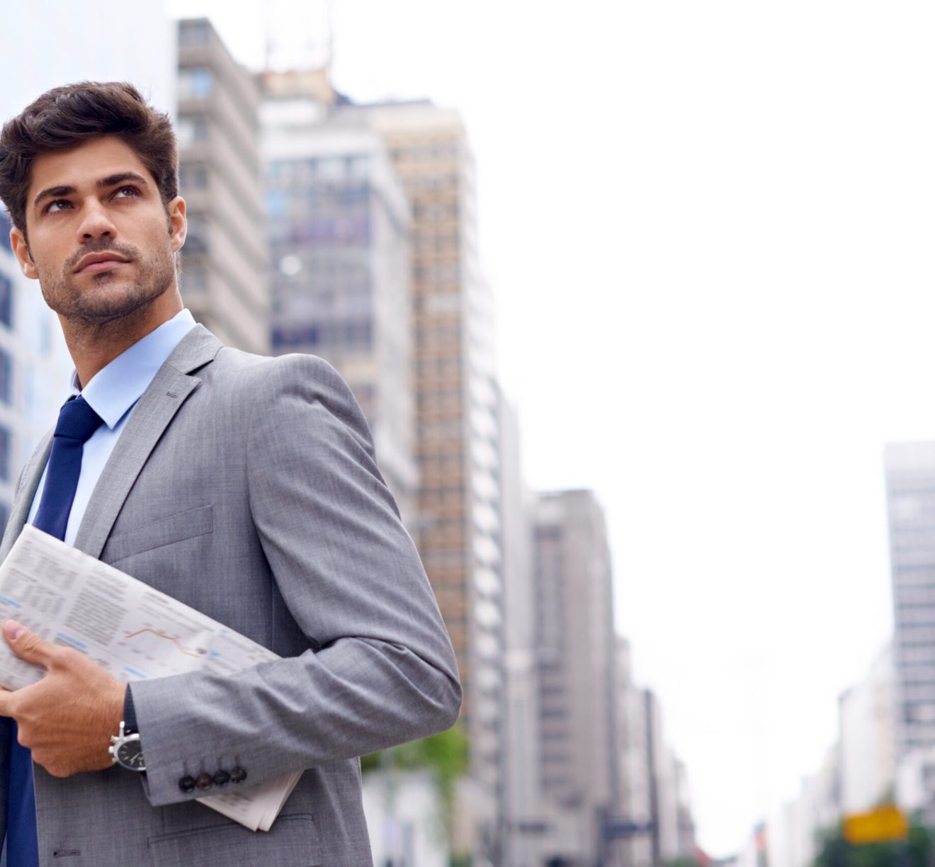 A handsome young businessman with a newspaper walking in the city.
